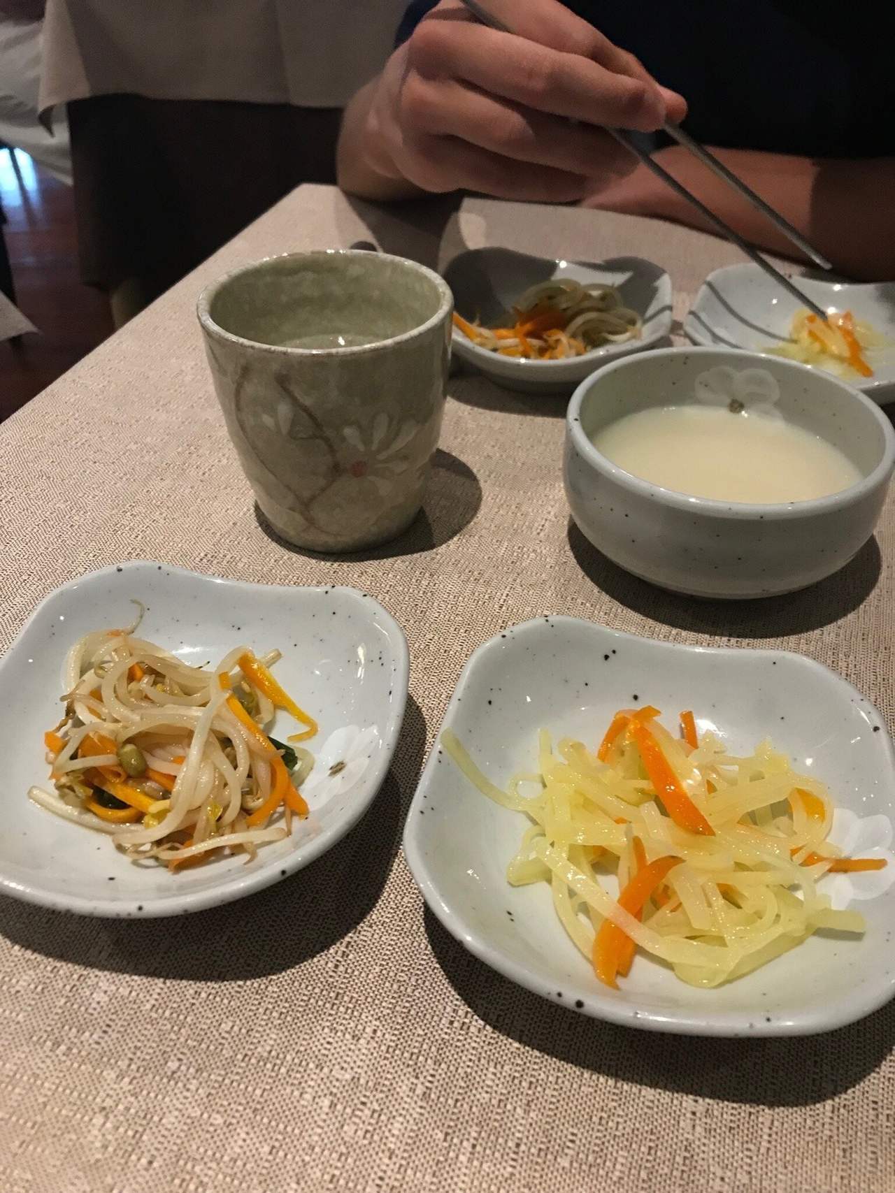 Banchan coreani in ciotoline bianche con tazze di tè, su una tavola del Dream