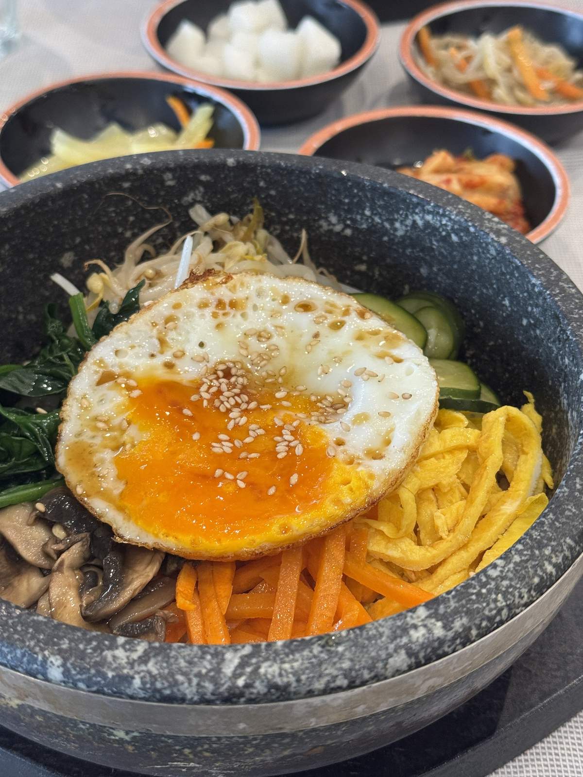 Dolsot bibimbap con uovo al tegamino, carote, frittata a listarelle e funghi, tra i banchan