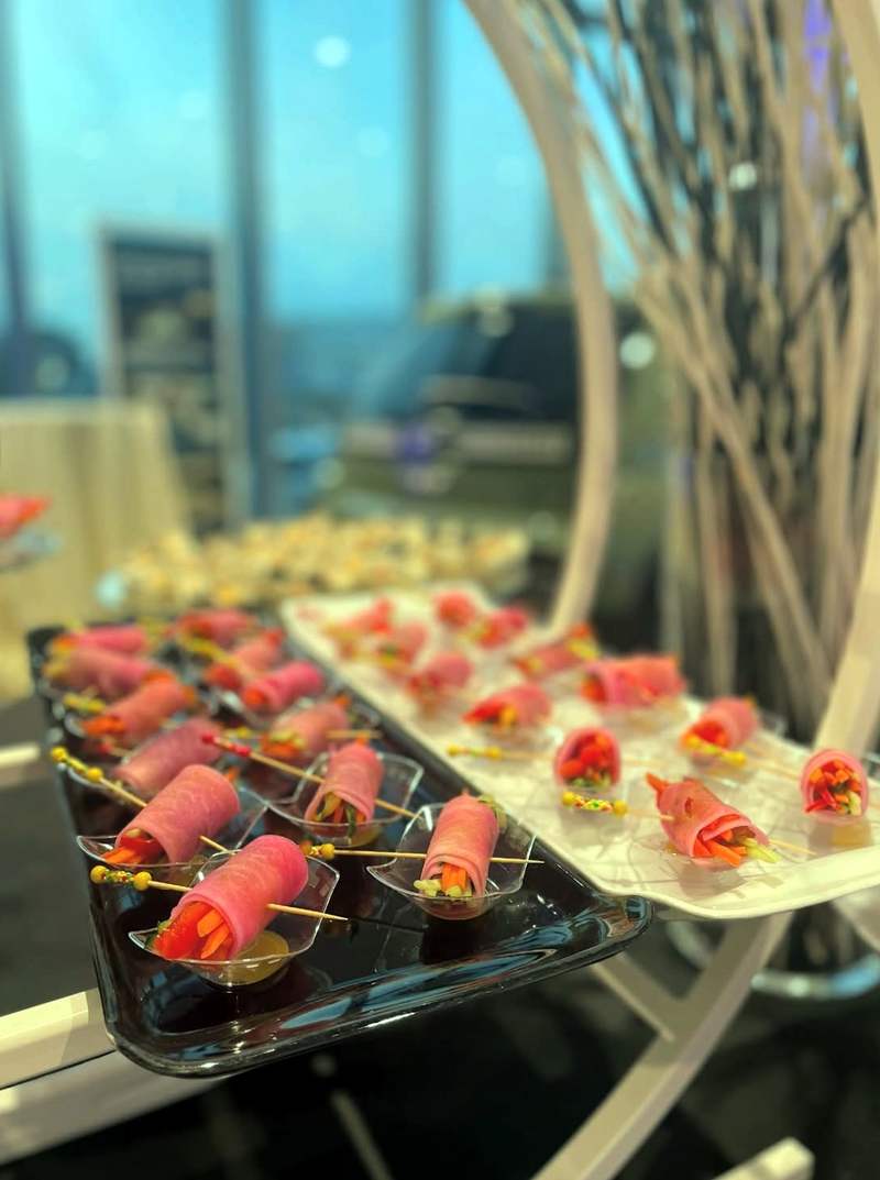 Involtini di daikon rosa con verdure su vassoi neri e bianchi, al buffet dell’evento
