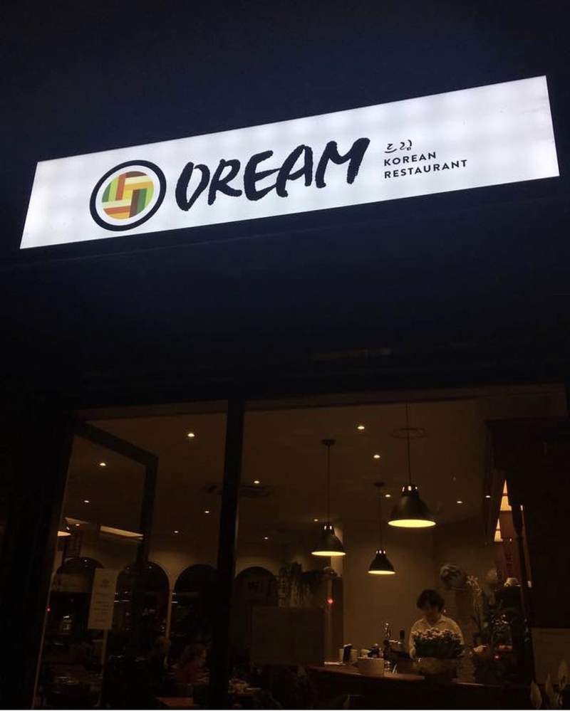 L’insegna illuminata DREAM Korean Restaurant di sera, con la sala accesa sotto