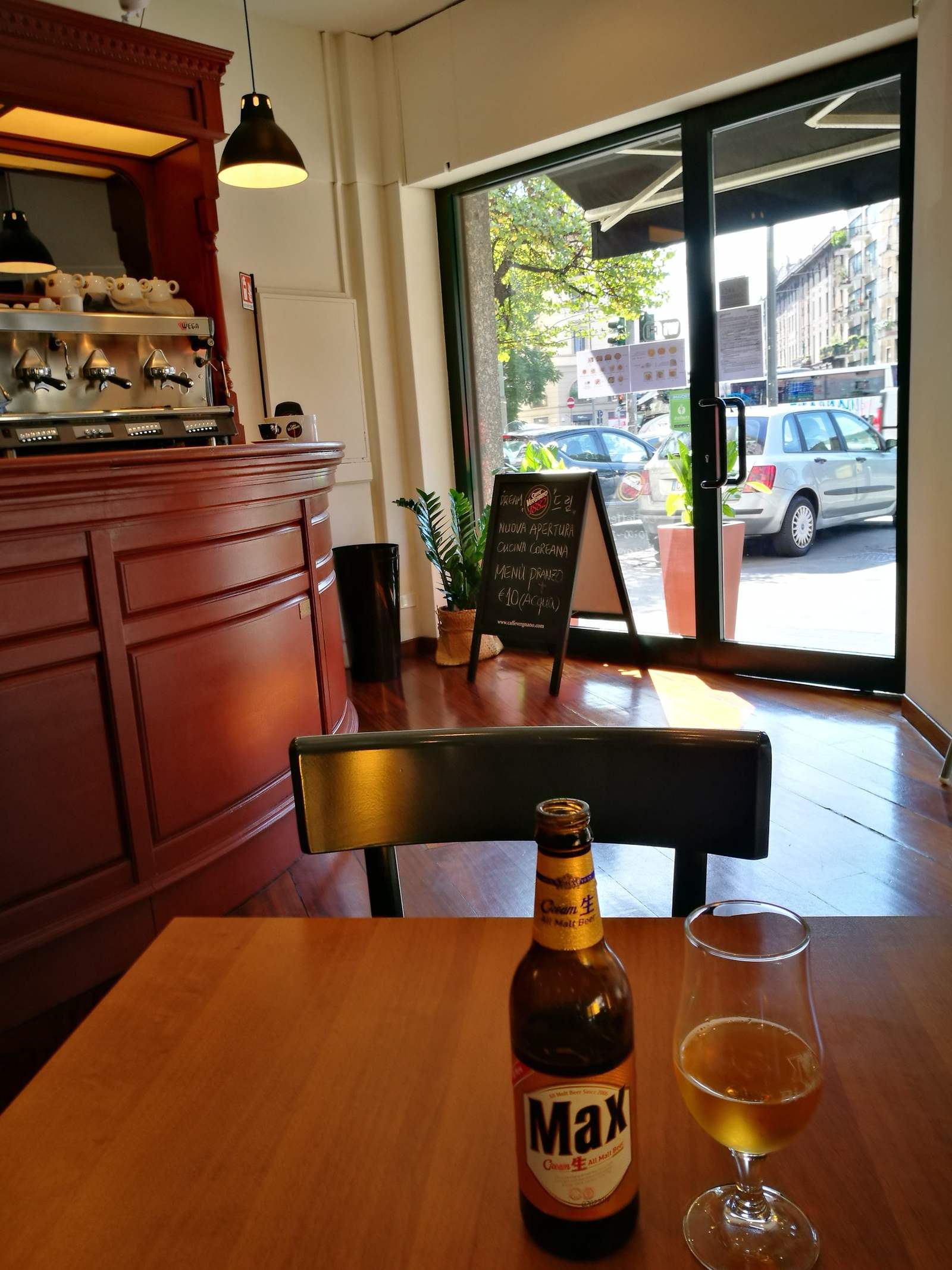 Bottiglia di birra coreana e bicchiere su un tavolo di legno nella sala del Dream, con la vetrata sulla piazza